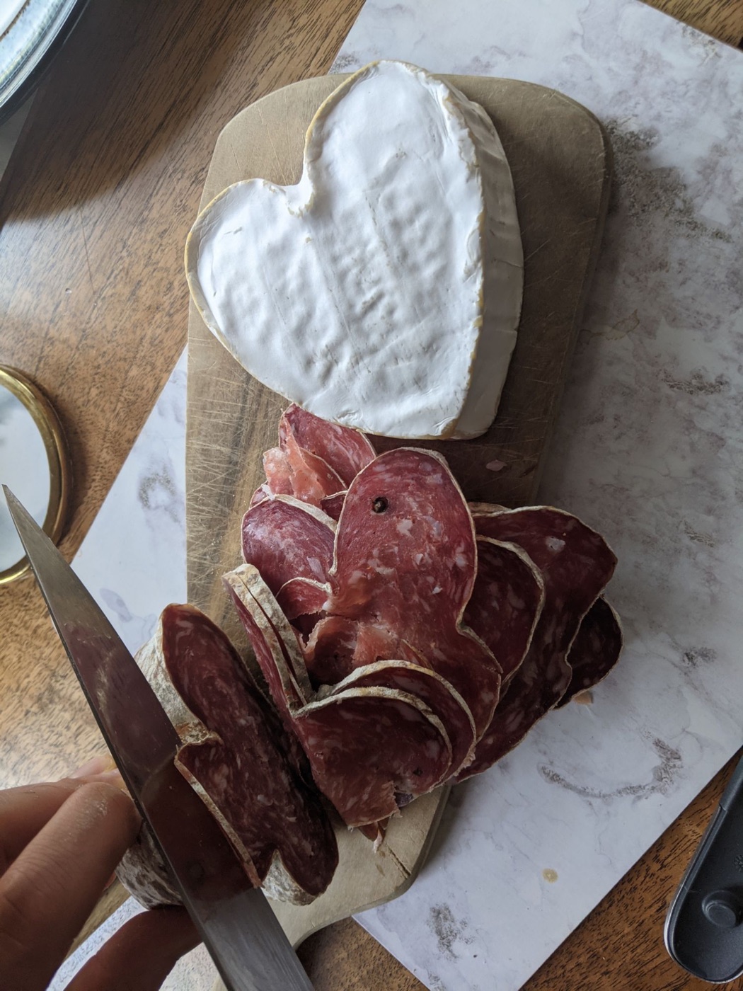 A heart-shaped cheese and sliced salami on a wooden board, mid-preparation for a Friday dinner