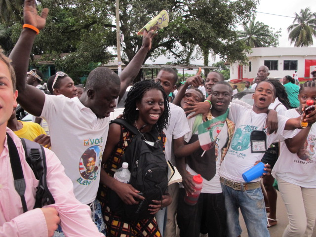 Dayo smiling in a crowd of young campaign supporters in Ellen Johnson Sirleaf T-shirts in Monrovia