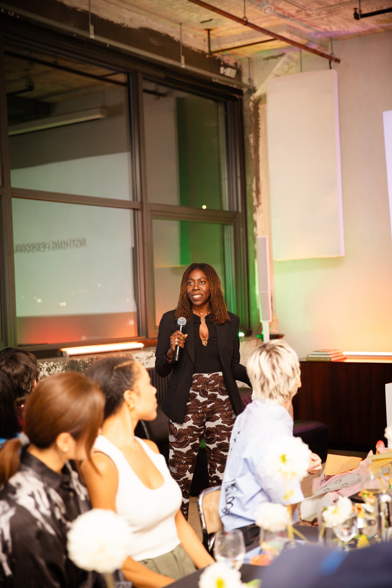 Dayo speaking with a microphone to a seated audience at the Nothing Personal launch