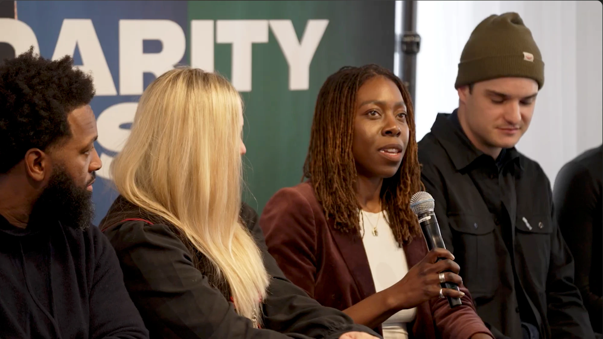 Dayo speaking into a microphone on the panel Is Technology Shaping Human Control? at the Sundance Film Festival, between Valerie Veatch and Charlie Tyrell
